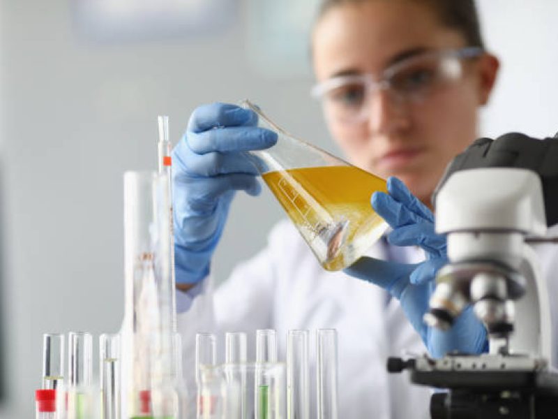 Woman chemist holds flask with yellow liquid in her hands in chemical laboratory. Quality control of petrochemical products concept.